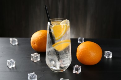 Photo of Refreshing soda water with orange slices and ice cubes on black wooden table