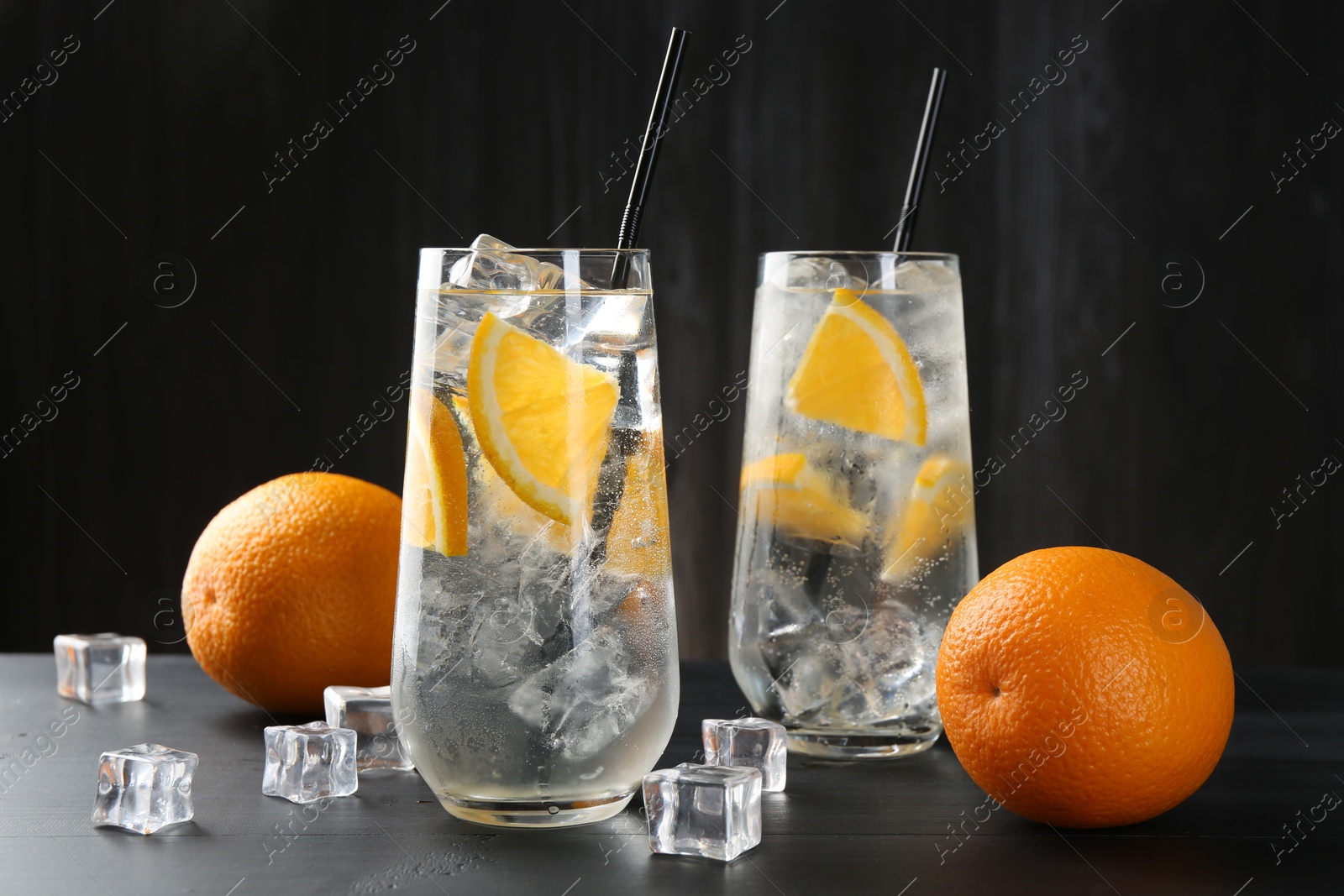 Photo of Refreshing soda water with orange slices and ice cubes on black wooden table, closeup