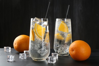 Photo of Refreshing soda water with orange slices and ice cubes on black wooden table, closeup