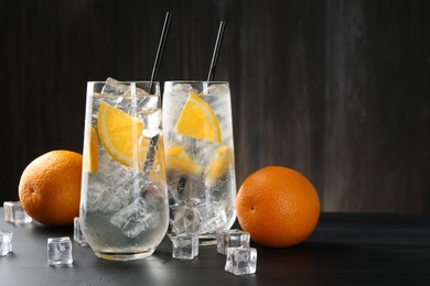 Photo of Refreshing soda water with orange slices and ice cubes on black wooden table. Space for text
