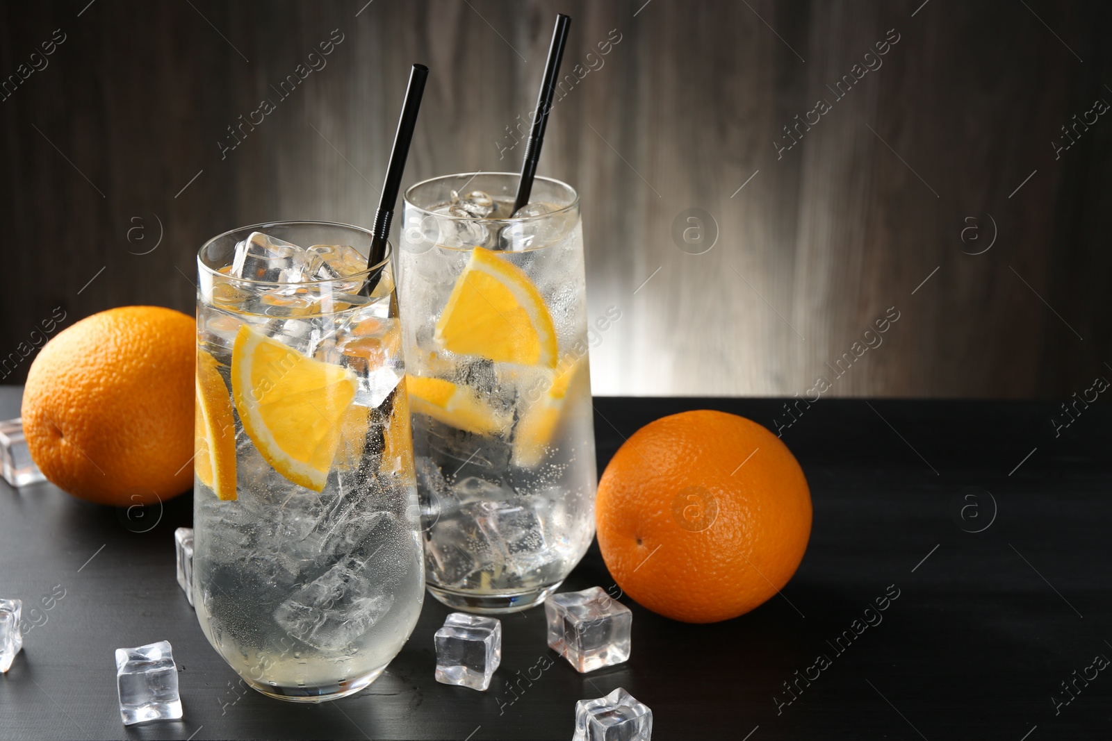 Photo of Refreshing soda water with orange slices and ice cubes on black wooden table, closeup. Space for text