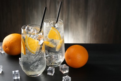 Photo of Refreshing soda water with orange slices and ice cubes on black wooden table, closeup. Space for text