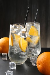 Photo of Refreshing soda water with orange slices and ice cubes on black wooden table, closeup
