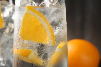 Photo of Refreshing soda water with orange slices and ice cubes in glasses on blurred background, closeup