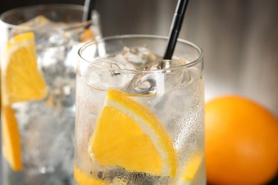 Photo of Refreshing soda water with orange slices and ice cubes in glasses on blurred background, closeup