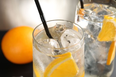Photo of Refreshing soda water with orange slices and ice cubes in glasses on blurred background, closeup