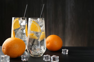 Photo of Refreshing soda water with orange slices and ice cubes on black wooden table, closeup. Space for text