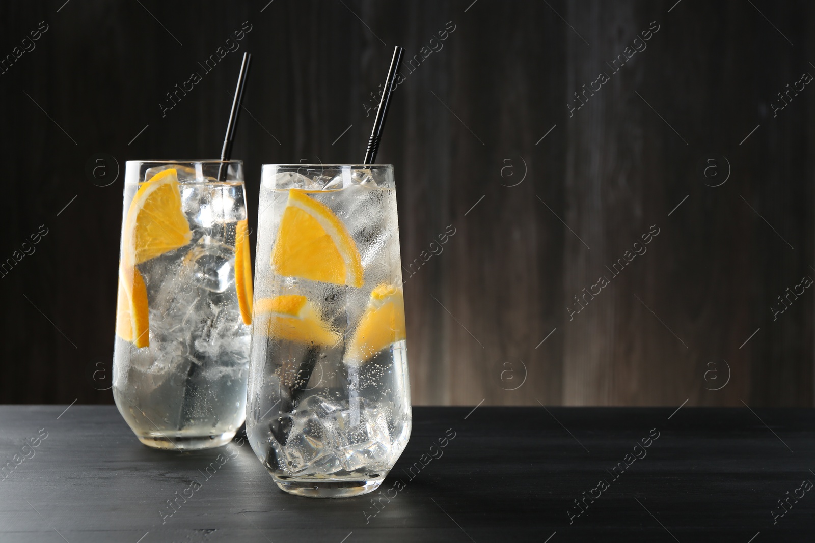 Photo of Refreshing soda water with orange slices and ice cubes in glasses on black wooden table. Space for text