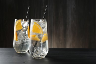 Photo of Refreshing soda water with orange slices and ice cubes in glasses on black wooden table. Space for text