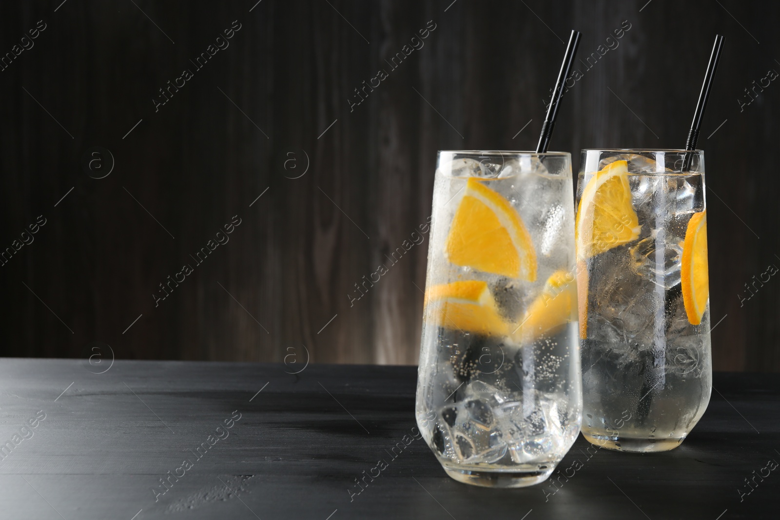 Photo of Refreshing soda water with orange slices and ice cubes in glasses on black wooden table. Space for text