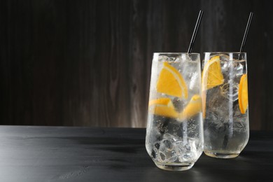 Photo of Refreshing soda water with orange slices and ice cubes in glasses on black wooden table. Space for text