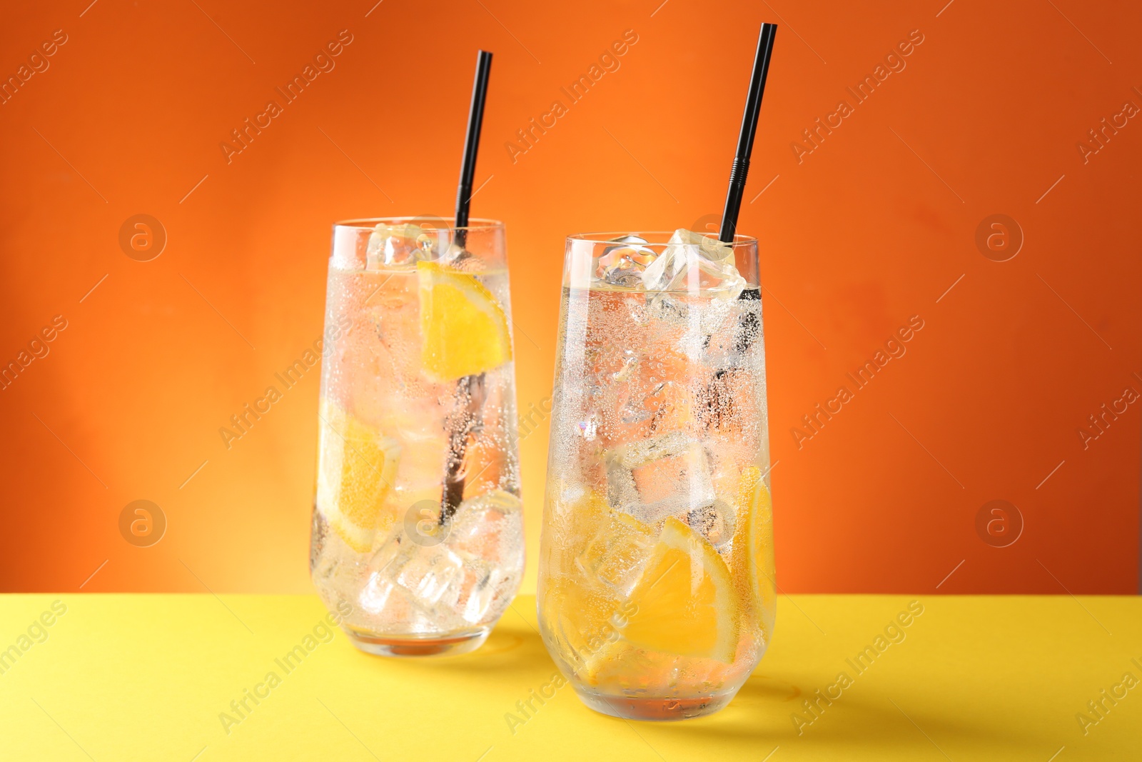 Photo of Refreshing soda water with orange slices and ice cubes in glasses on yellow table against orange background