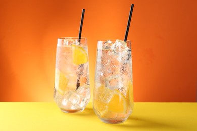 Photo of Refreshing soda water with orange slices and ice cubes in glasses on yellow table against orange background