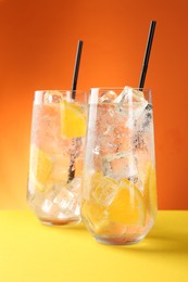 Photo of Refreshing soda water with orange slices and ice cubes in glasses on yellow table against orange background