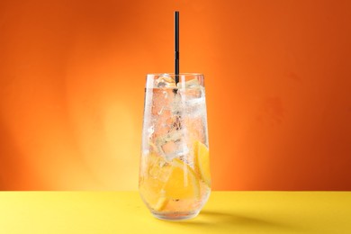 Photo of Refreshing soda water with orange slices and ice cubes in glass on yellow table against orange background