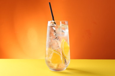 Photo of Refreshing soda water with orange slices and ice cubes in glass on yellow table against orange background