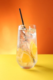 Photo of Refreshing soda water with orange slices and ice cubes in glass on yellow table against orange background