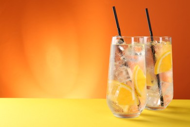 Photo of Refreshing soda water with orange slices and ice cubes in glasses on yellow table against orange background. Space for text