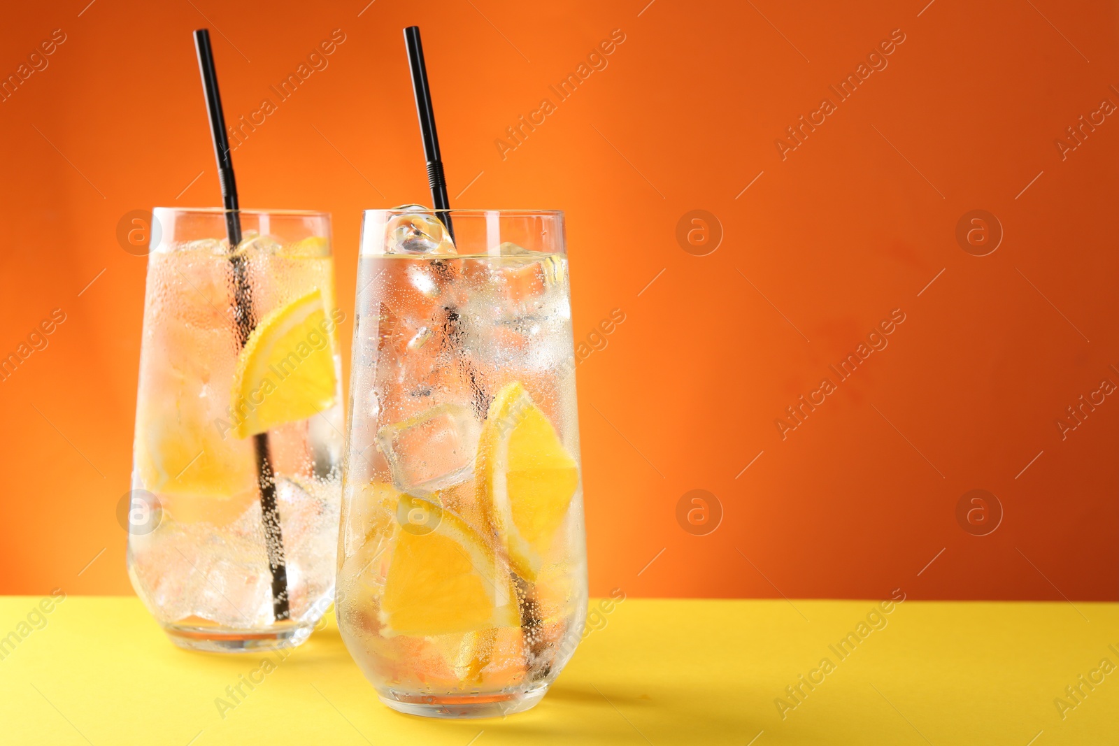 Photo of Refreshing soda water with orange slices and ice cubes in glasses on yellow table against orange background. Space for text
