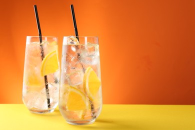 Photo of Refreshing soda water with orange slices and ice cubes in glasses on yellow table against orange background. Space for text