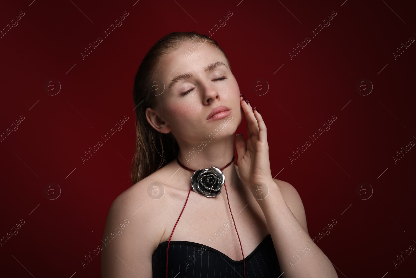 Photo of Beautiful woman in stylish necklace posing on dark red background