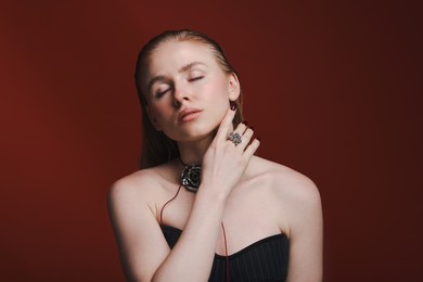 Photo of Beautiful woman in stylish necklace and ring posing on dark red background