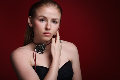 Photo of Fashionable portrait of beautiful woman in stylish necklace and ring posing on dark red background. Space for text