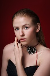 Photo of Fashionable portrait of beautiful woman in stylish necklace posing on dark red background