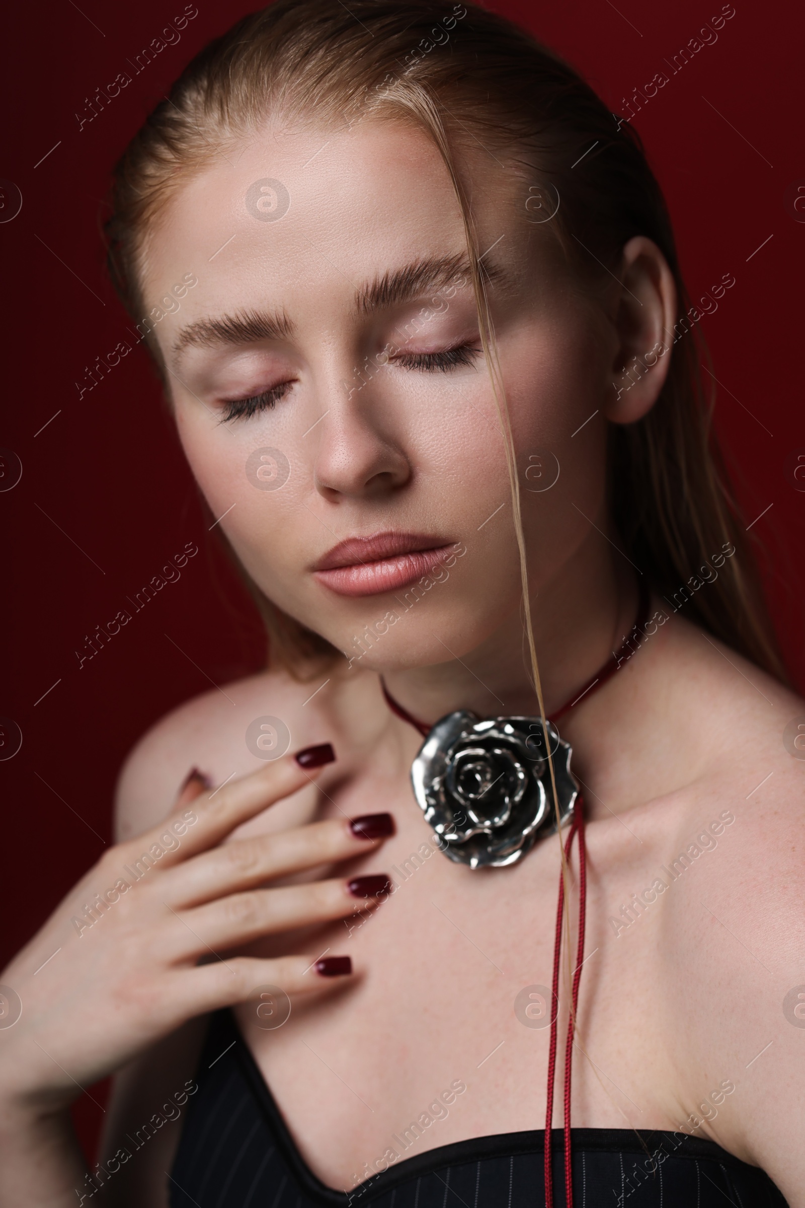 Photo of Beautiful woman in stylish necklace posing on dark red background, closeup