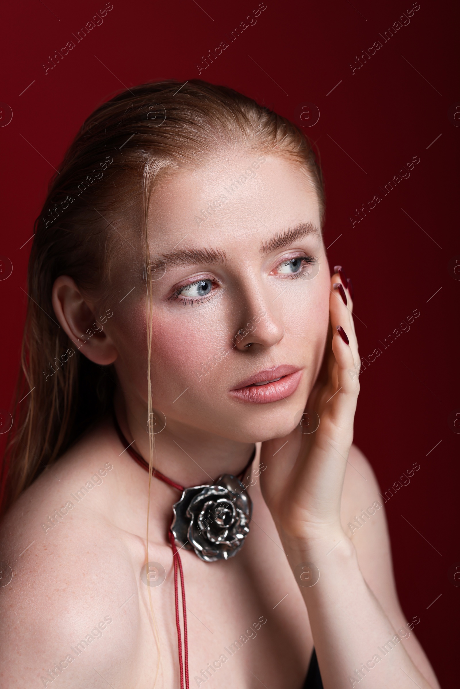 Photo of Beautiful woman in stylish necklace posing on dark red background, closeup
