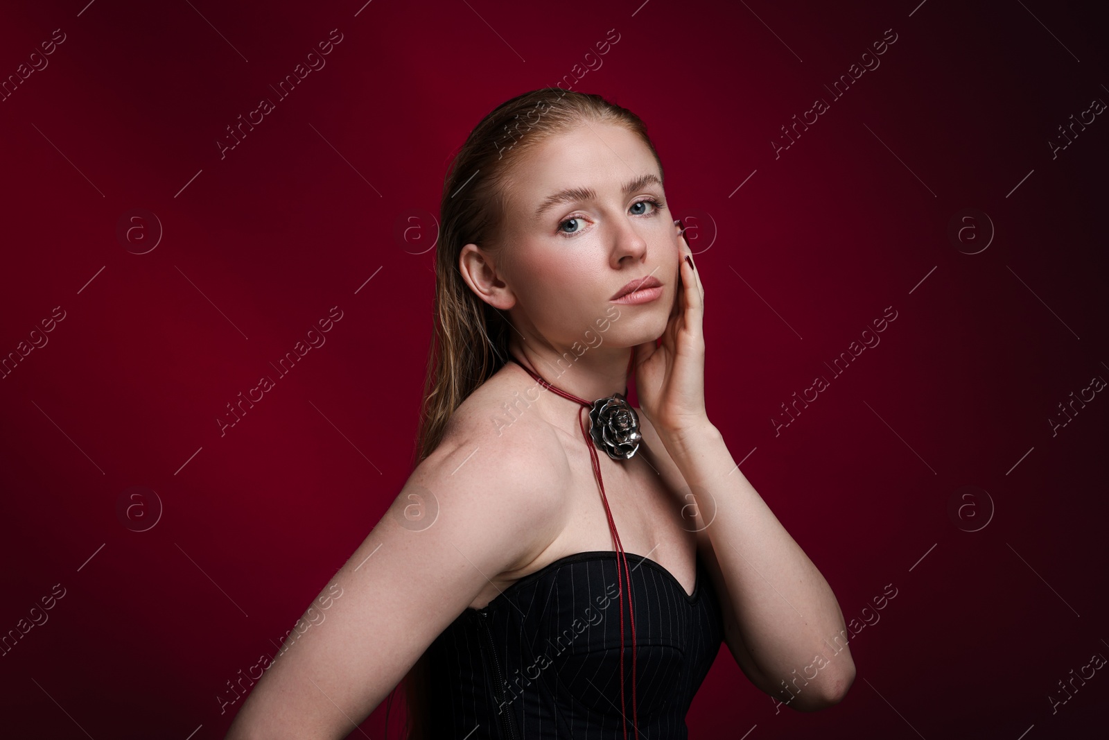 Photo of Fashionable portrait of beautiful woman in stylish necklace posing on dark red background
