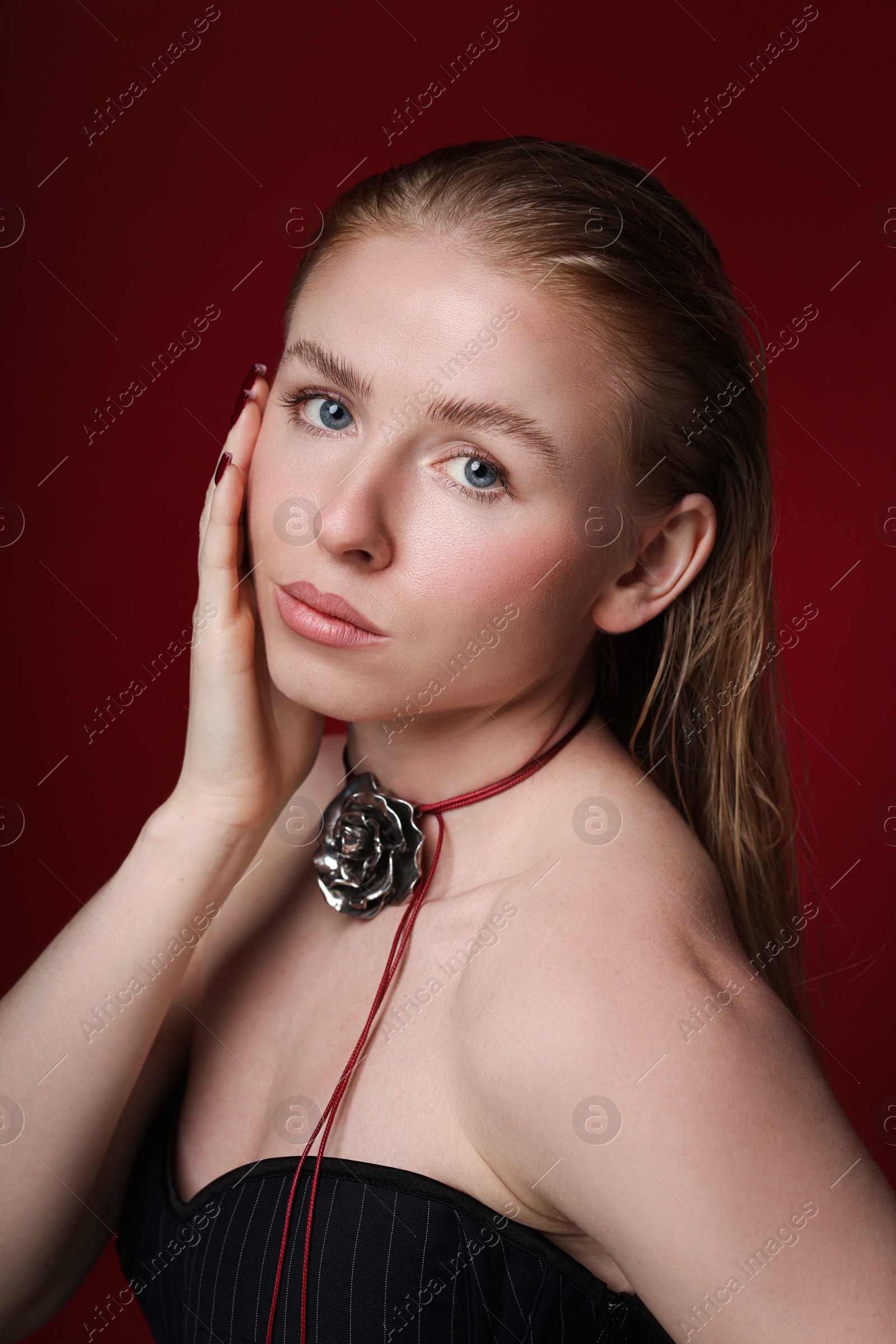 Photo of Fashionable portrait of beautiful woman in stylish necklace posing on dark red background