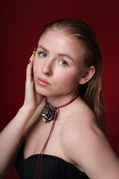 Photo of Fashionable portrait of beautiful woman in stylish necklace posing on dark red background