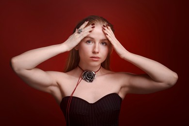 Photo of Fashionable portrait of beautiful woman in stylish necklace and ring posing on dark red background