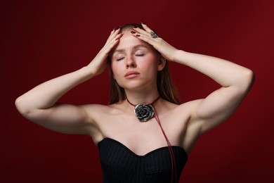 Photo of Beautiful woman in stylish necklace and ring posing on dark red background