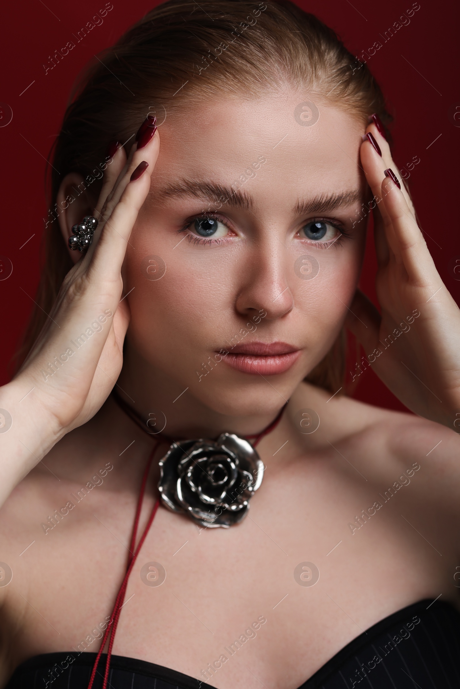 Photo of Fashionable portrait of beautiful woman in stylish necklace and ring posing on dark red background, closeup