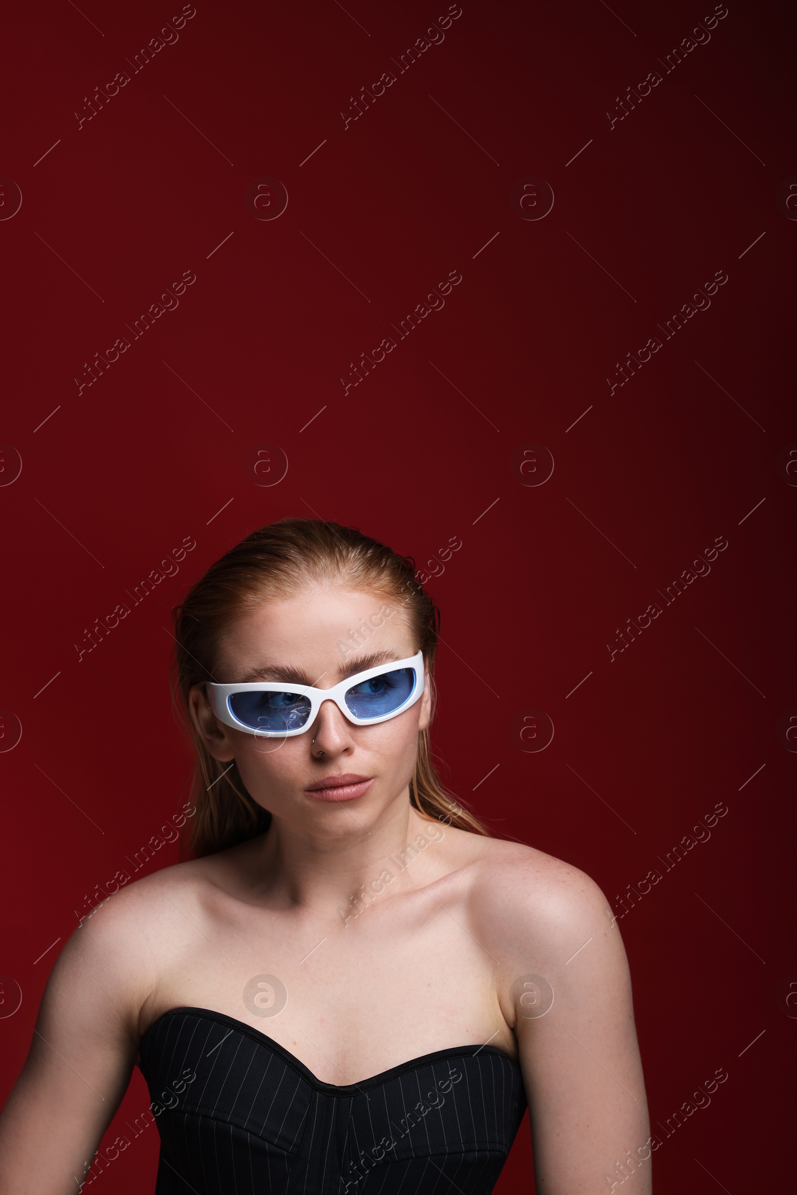 Photo of Beautiful woman in stylish sunglasses posing on dark red background