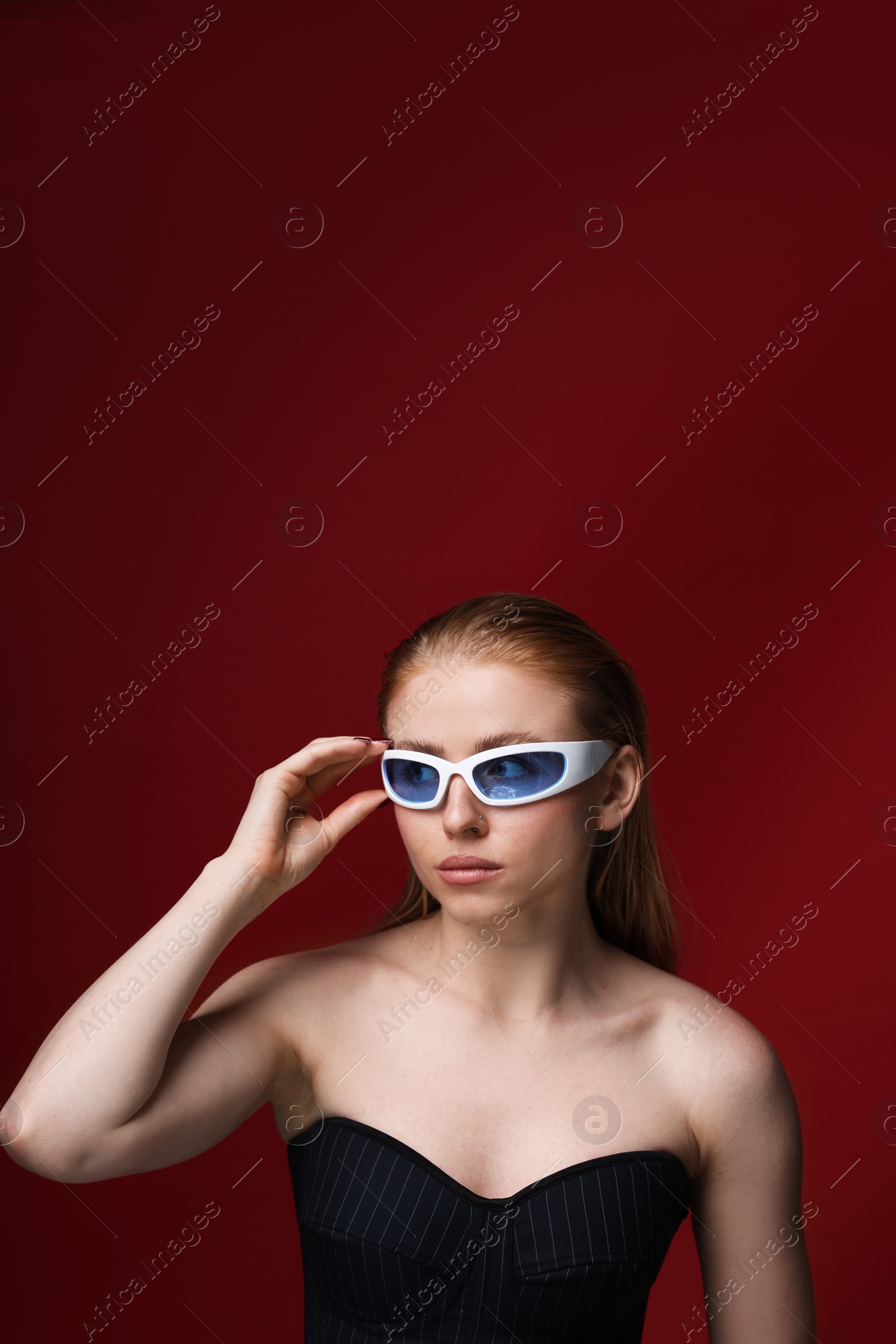 Photo of Beautiful woman in stylish sunglasses posing on dark red background
