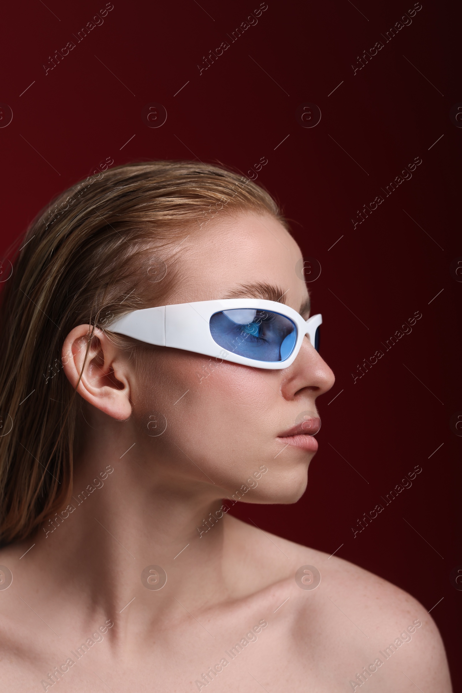 Photo of Beautiful woman in stylish sunglasses posing on dark red background