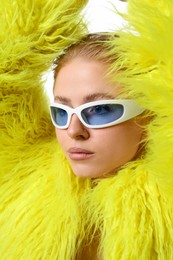 Photo of Beautiful woman in stylish sunglasses and fur coat posing on white background, closeup