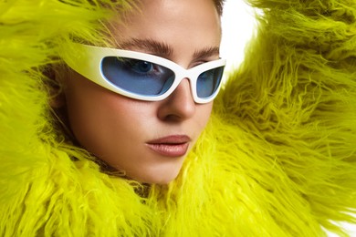 Photo of Beautiful woman in stylish sunglasses and fur coat posing on white background, closeup