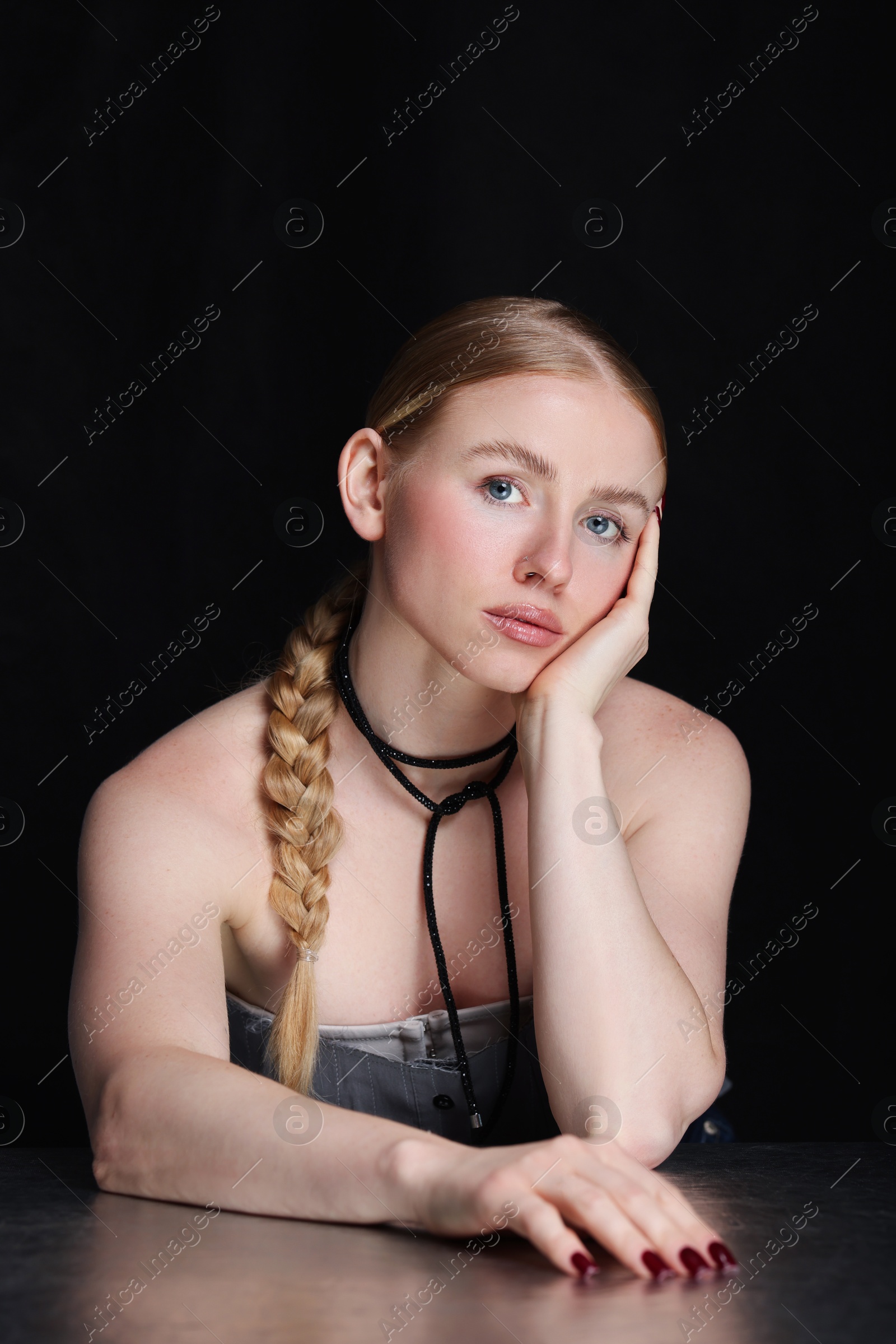 Photo of Fashionable portrait of beautiful woman with pigtail posing at table on black background