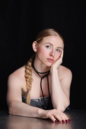 Photo of Fashionable portrait of beautiful woman with pigtail posing at table on black background