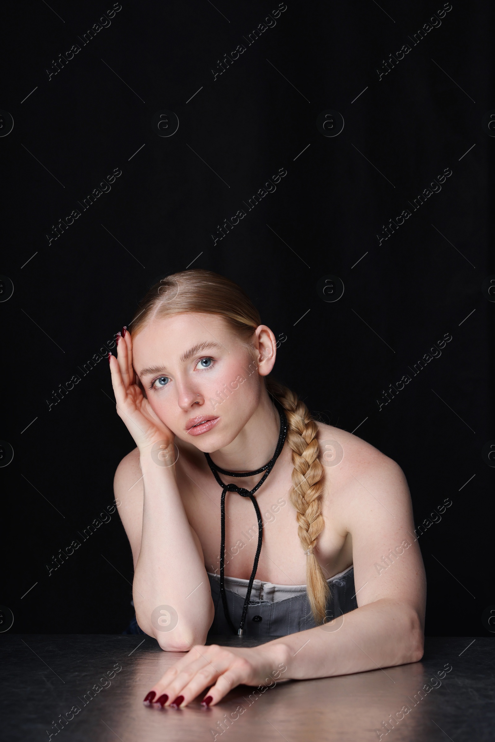 Photo of Fashionable portrait of beautiful woman with pigtail posing at table on black background