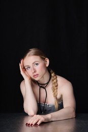 Photo of Fashionable portrait of beautiful woman with pigtail posing at table on black background