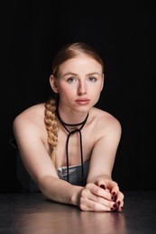 Photo of Fashionable portrait of beautiful woman with pigtail posing at table on black background