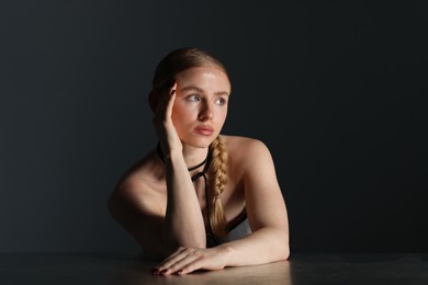 Photo of Beautiful woman with pigtail posing at table on dark background