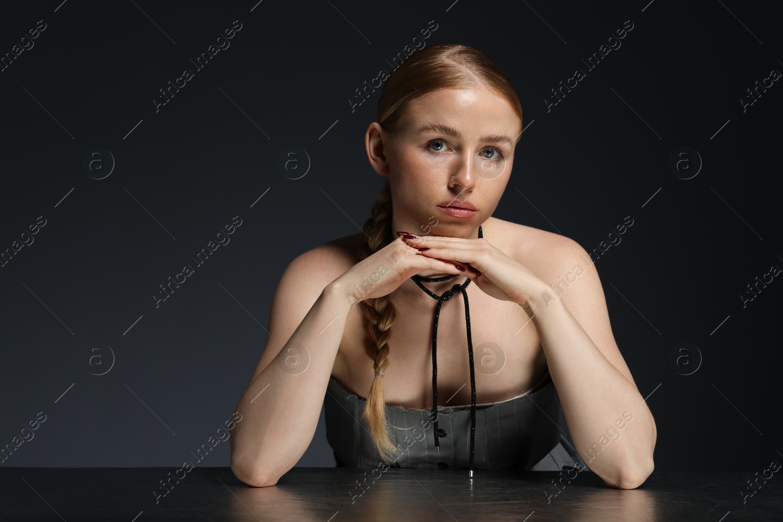 Photo of Fashionable portrait of beautiful woman with pigtail posing at table on dark grey background