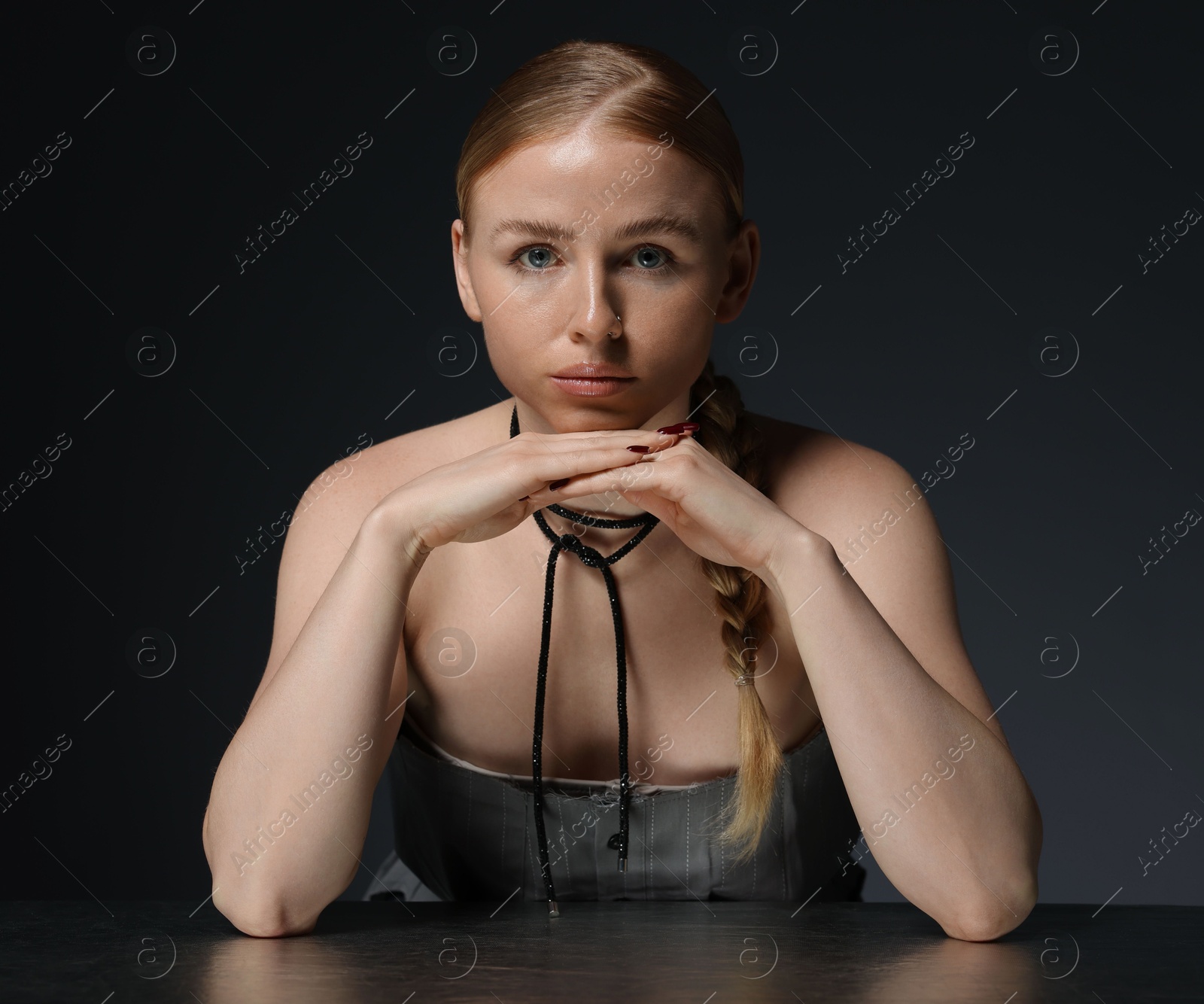 Photo of Fashionable portrait of beautiful woman with pigtail posing at table on dark grey background