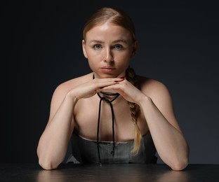 Photo of Fashionable portrait of beautiful woman with pigtail posing at table on dark grey background